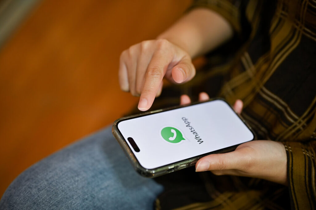 Mãos femininas segurando um celular com a logo do WhatsApp enquanto acessa o SAC da empresa.