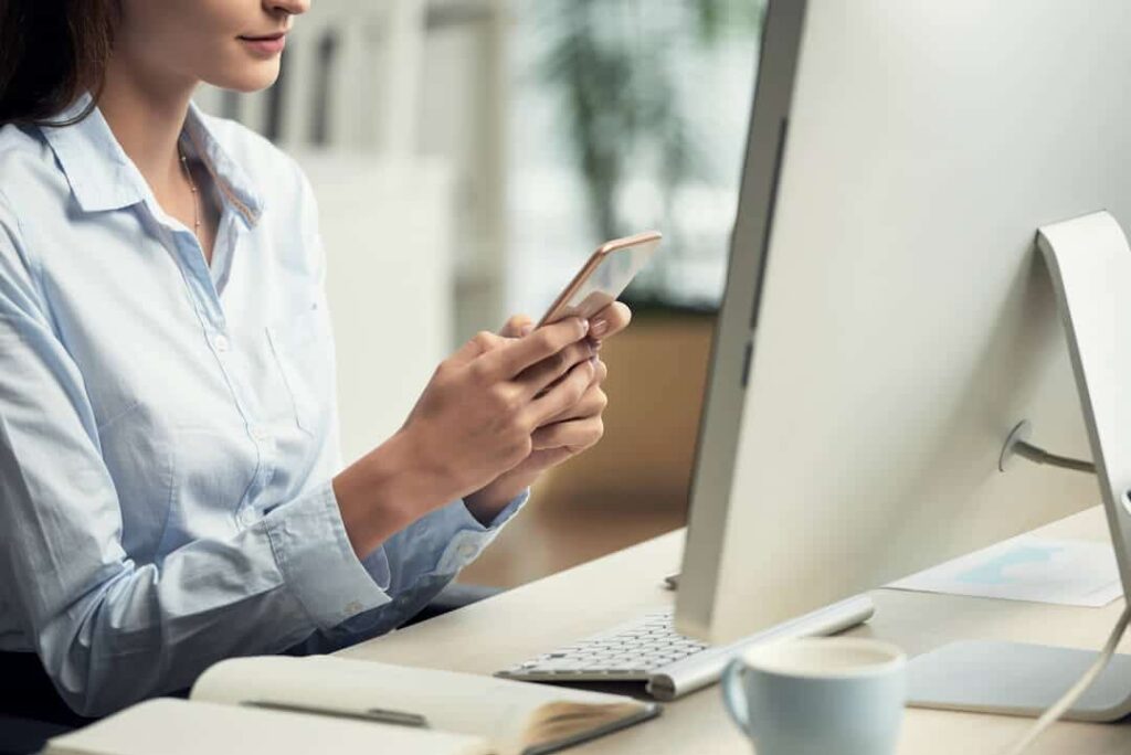 Mulher acessando seu aplicativo do WhatsApp Business enquanto pesquisa sobre o WhatsApp Business API no computador.