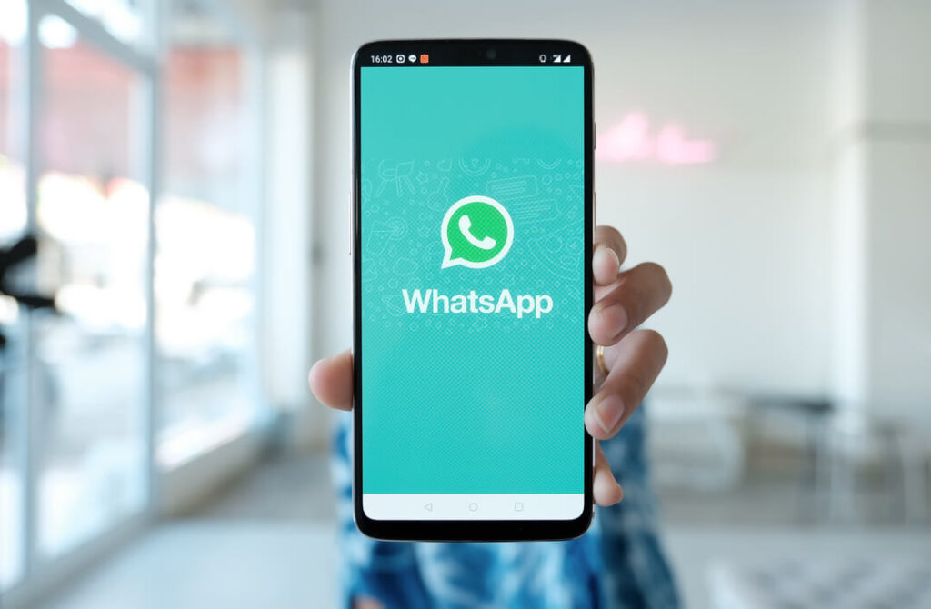 Mulher segurando smartphone com tela do WhatsApp, que será sua estratégia para as vendas de final de ano.