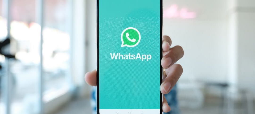 Mulher segurando smartphone com tela do WhatsApp, que será sua estratégia para as vendas de final de ano.