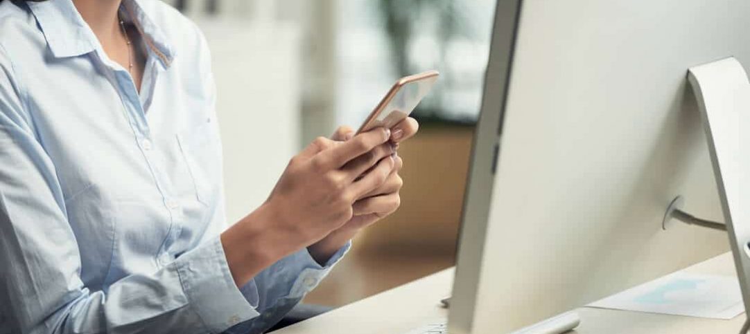 Mulher acessando seu aplicativo do WhatsApp Business enquanto pesquisa sobre o WhatsApp Business API no computador.