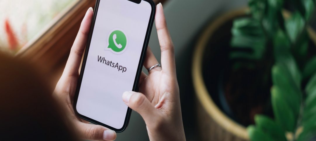 Mulher segudando celular com logo do WhatsApp na tela que representa a criação de mensagem automática no WhatsApp.